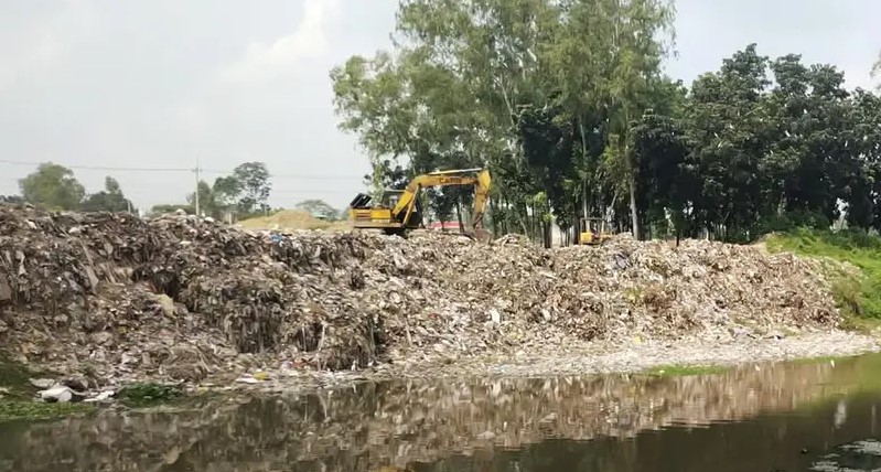 করতোয়া নদীর তীরে জমে থাকা বিপুল পরিমাণ নগর বর্জ্য সরাচ্ছে এক্সকেভেটর।